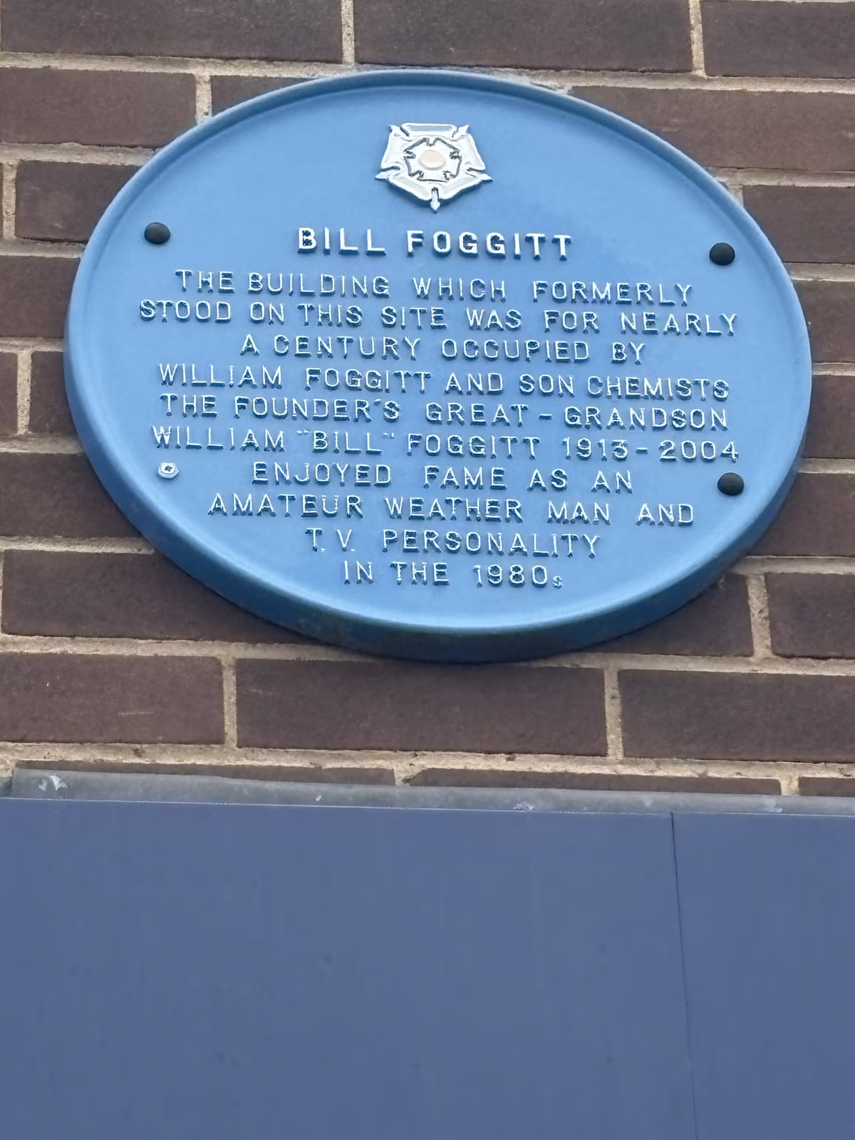 The blue plaque to Bill Foggitt on the brick wall of Boots in Thirsk Market Place, recording the chemist's shop that stood on the site and Foggitt's fame as a television weather forecaster