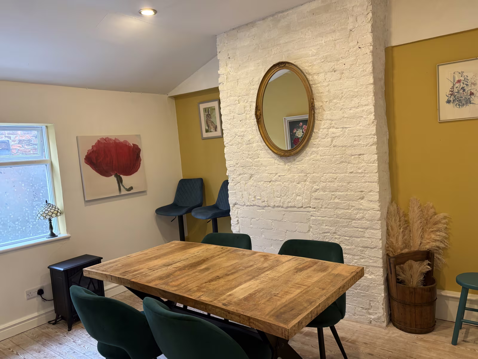 The back room upstairs at Tea Time, a wooden table with green chairs against a whitewashed brick chimney breast and a round mirror
