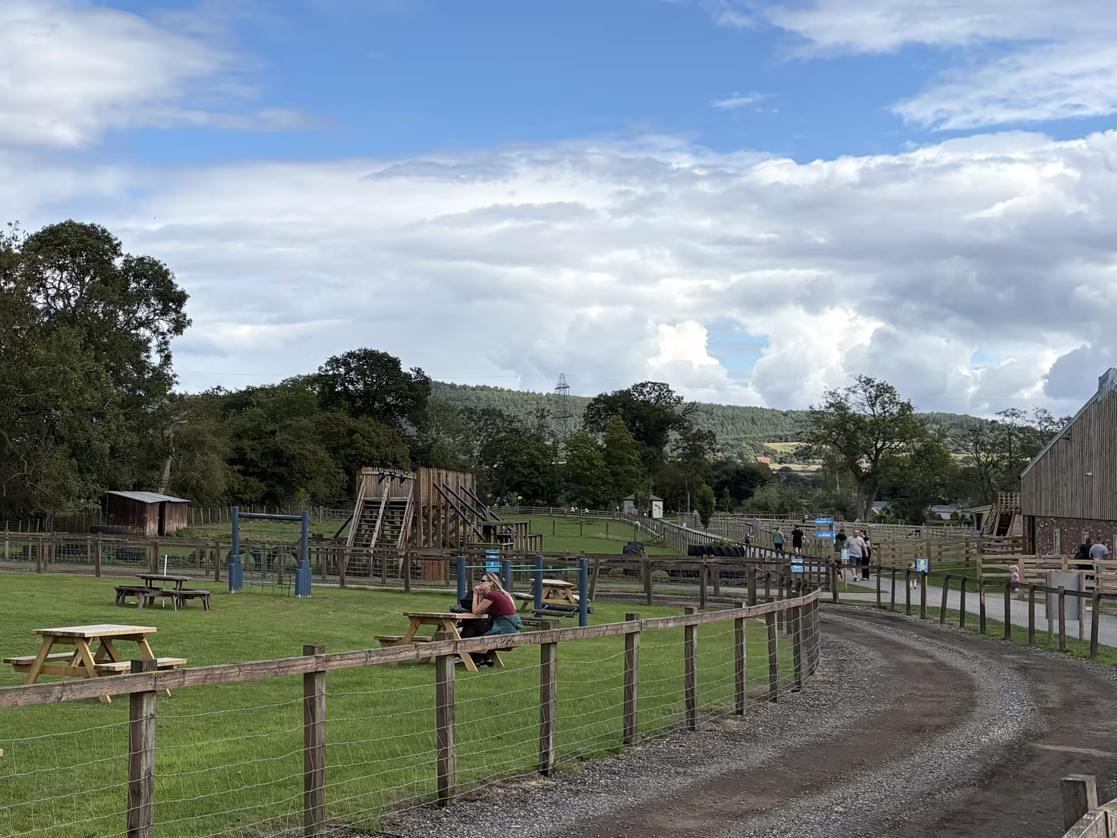The grass play field at Monk Park Farm with a wooden climbing fort, picnic tables and the hills behind