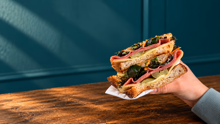 Two thick halves of Tea Time's Reuben, filled with pastrami, cheese, gherkins and slaw, held in one hand