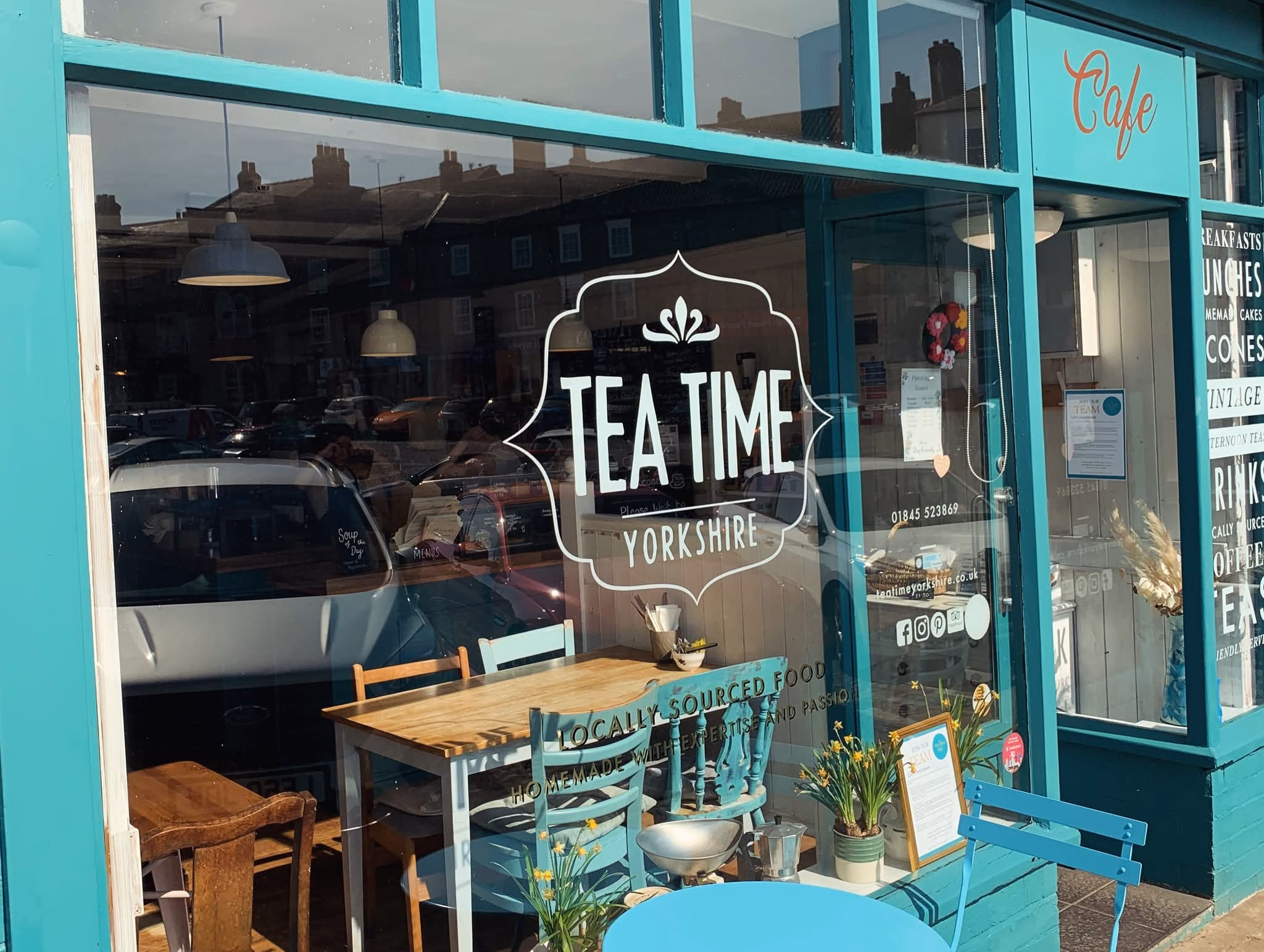 The Tea Time Cafe window on Thirsk market square with teal chairs and the open door