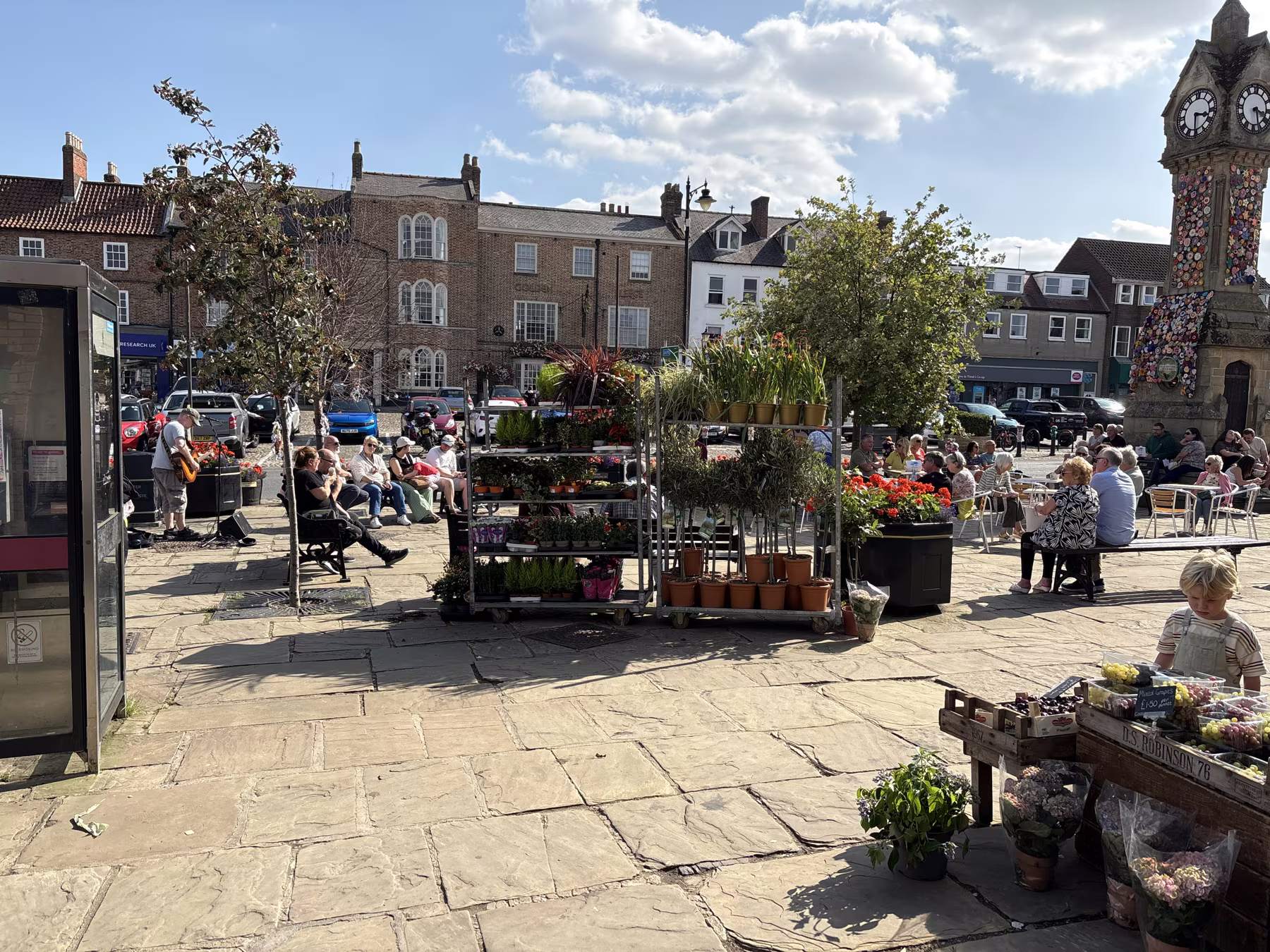 Stalls on Thirsk Market Place, with people sitting out at tables