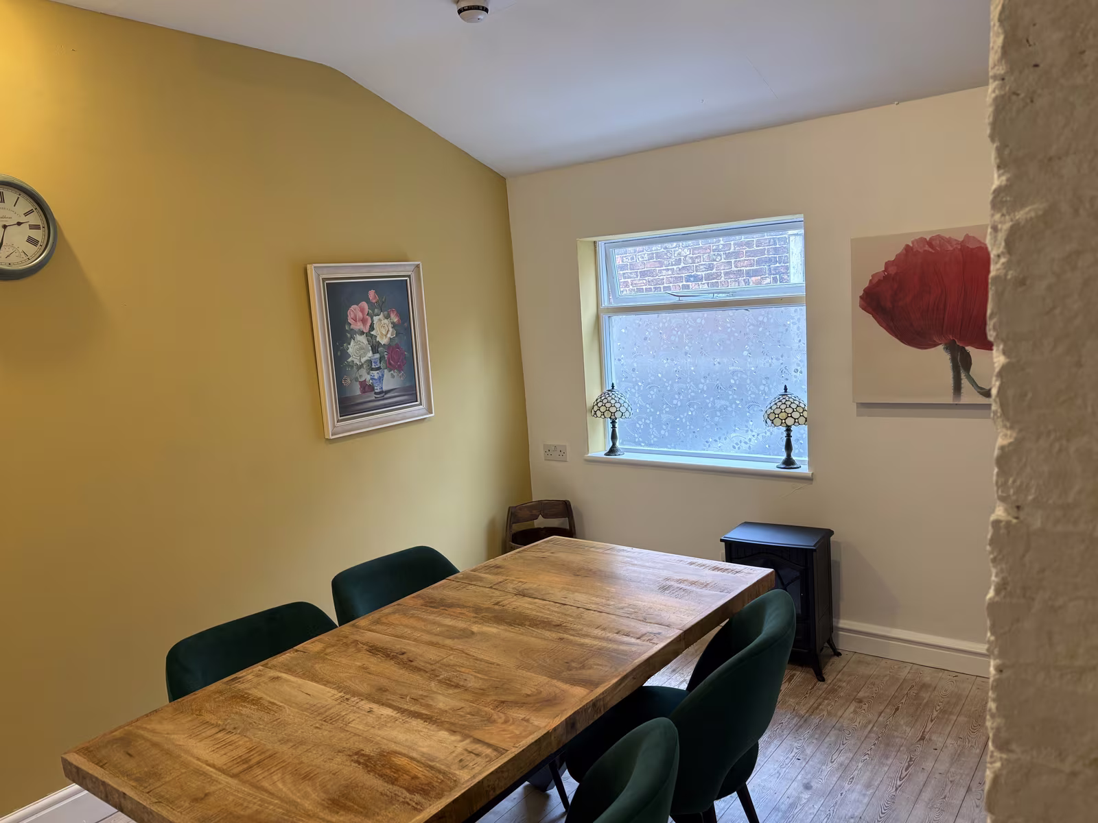The back room upstairs at Tea Time, a wooden table with green chairs under a window and a poppy painting on the yellow wall