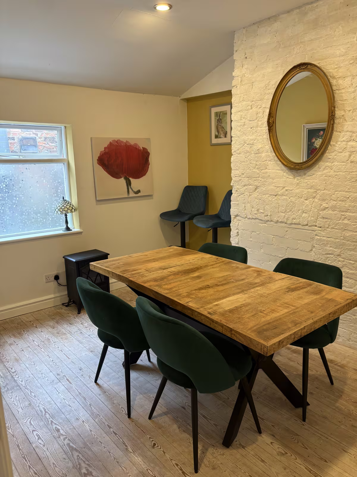 The private dining room upstairs at Tea Time from the doorway: whitewashed brick, a gilt oval mirror and green velvet chairs round the table